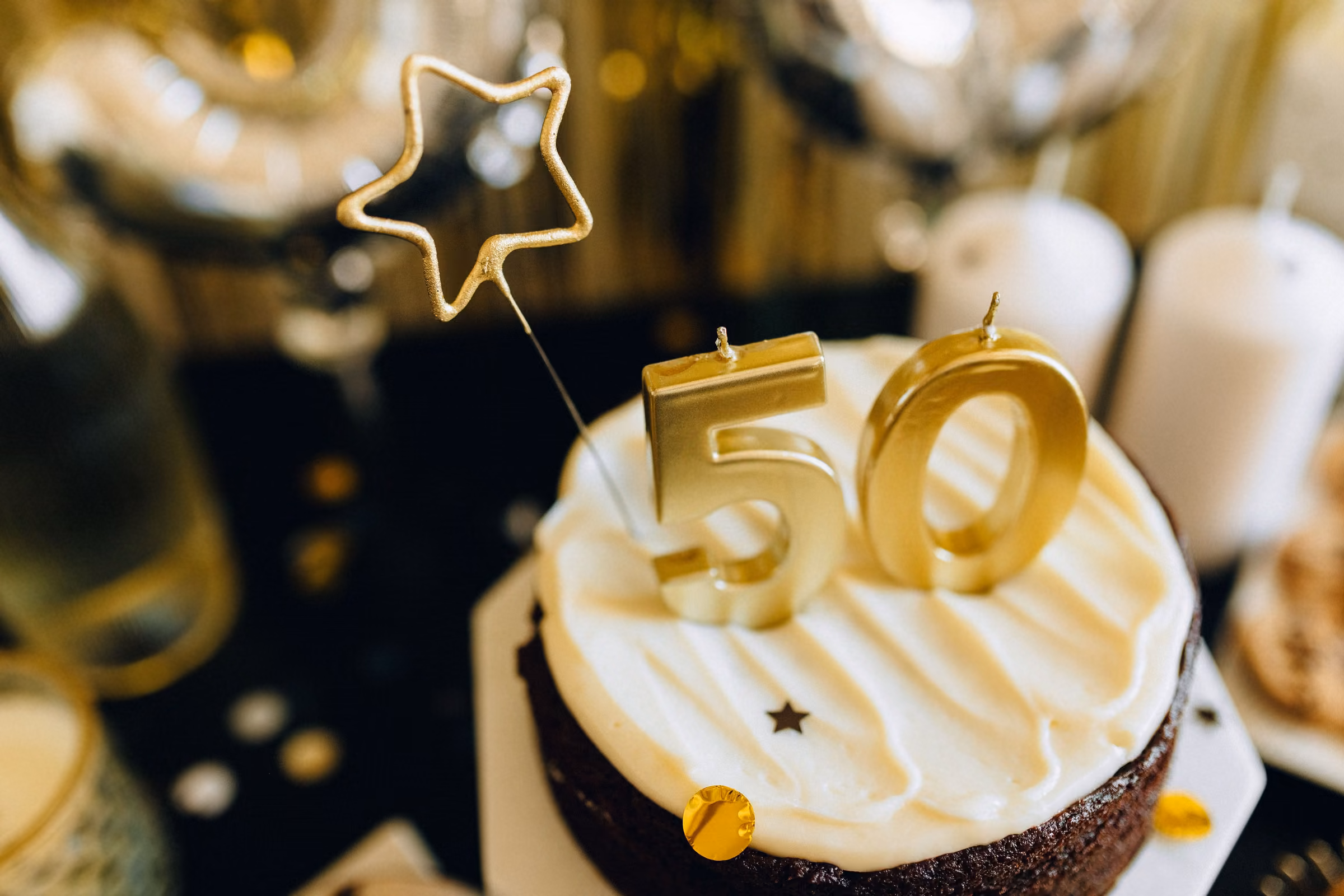 Юбилейный торт со свечой-цифрой 50 среди золотых шаров на тёмном фоне